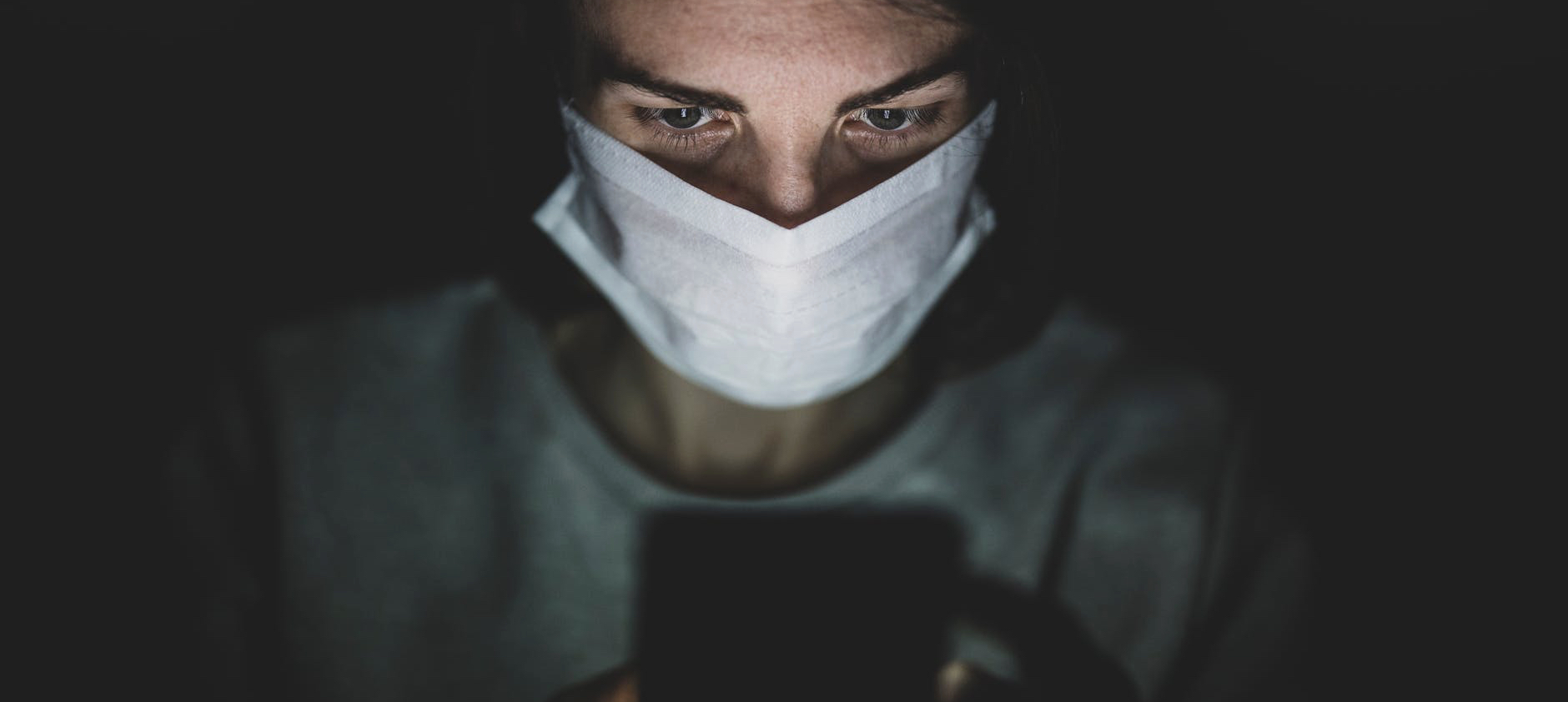 man wearing face mask using his phone in the dark