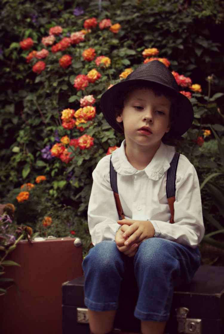 boy wearing black hat sitting on case near flowers